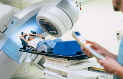 A patient lying with their arms raised as they receive radiation therapy in a linear accelerator. A technician stands nearby.