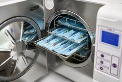 An autoclave is open and some of the trays are pulled partially out. The autoclave is full of packaged dental probes.