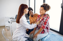  A doctor listening to a teenage patient's heartbeat through a stethoscope. The patient's guardian sits beside the patient.