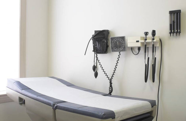 An exam table covered with protective paper is seen in a doctor's office. Various medical instruments are on the wall.