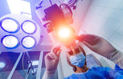 A masked surgeon is seen from the patient's perspective as she adjusts a laser to perform eye surgery.